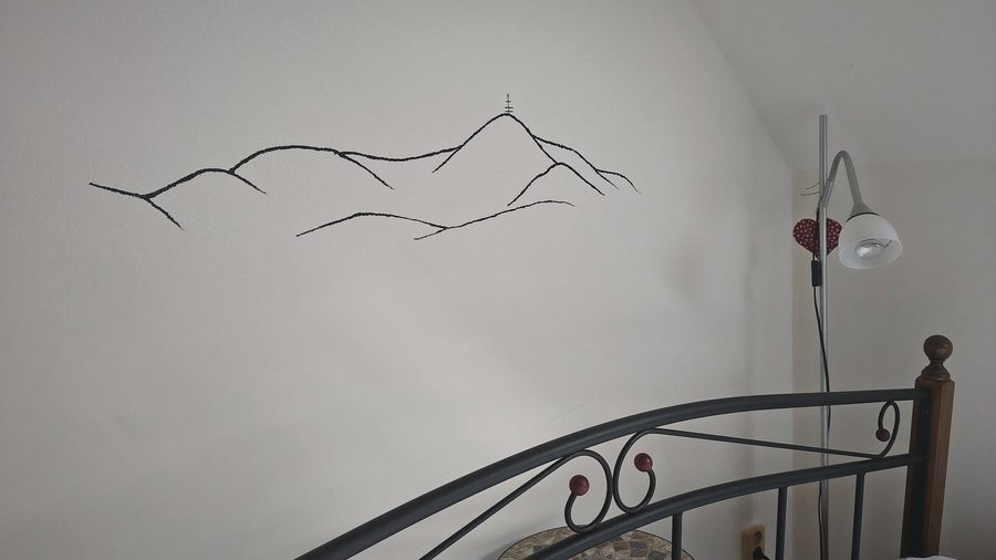 Tenká černá kresba obrysu hor na bílé zdi ložnice