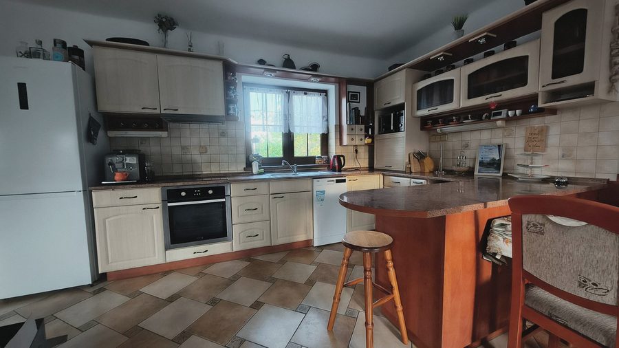 Kuchyně se světlými skříňkami, troubou a barovým pultem