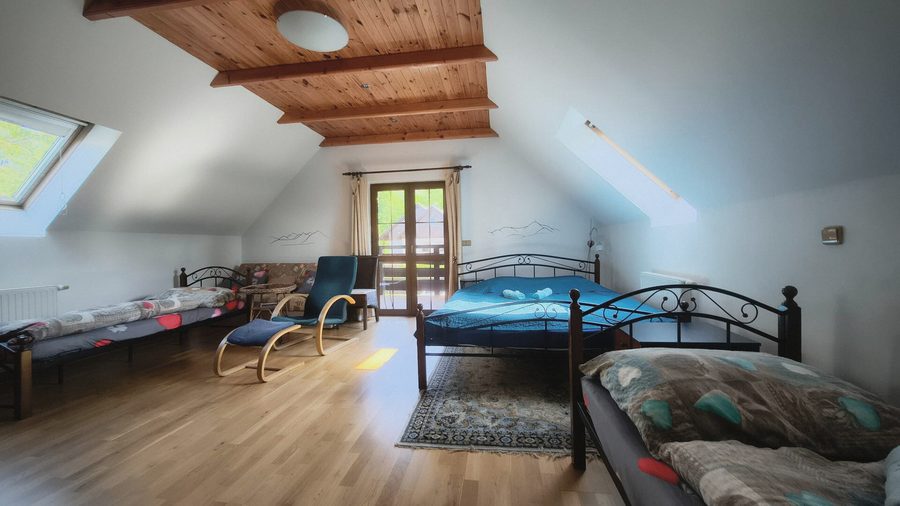 Podkrovní ložnice s kovovou postelí, křeslem a dveřmi na balkon