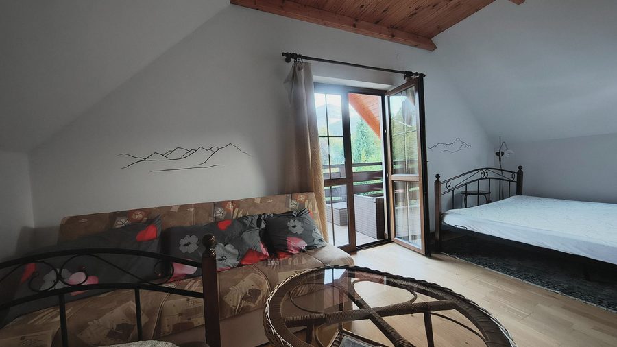 Postel u balkonových dveří, za nimi les a hory