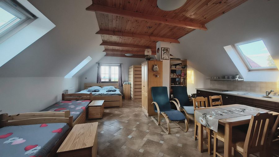 Velká podkrovní místnost s postelemi, střešními okny, stolem a kuchyňkou